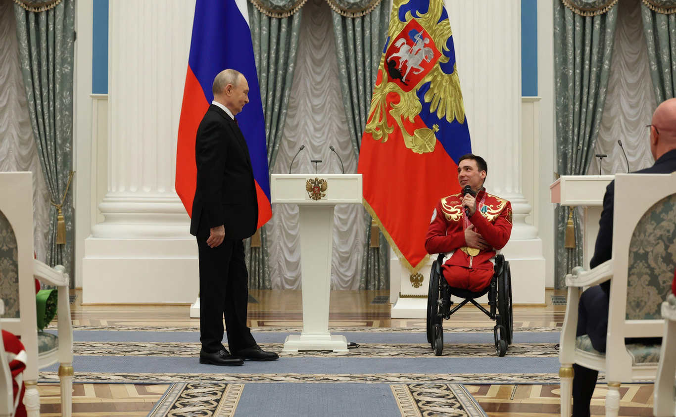 Владимир Путин поздравляет лыжника-паралимпийца Ивана Голубкова во время церемонии награждения российских спортсменов-паралимпийцев на зимних Олимпийских играх в Кремле. Москва, Россия. 19 марта 2026 года. Фото: Вячеслав Прокофьев / Alamy / Scanpix / LETA (edited)