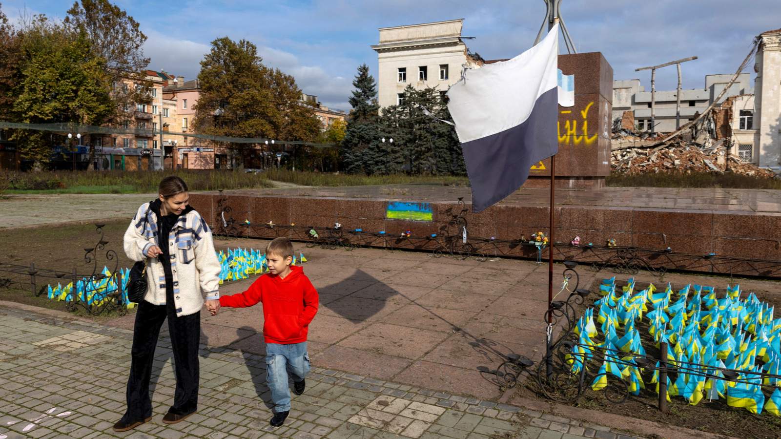 Местная жительница с сыном гуляют по центральной площади рядом с разрушенным зданием областной военной администрации. Херсон, Украина. 28 октября 2026 года. Фото: Thomas Peter / Reuters / Scanpix / LETA
