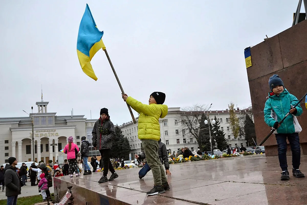 Дети машут украинскими флагами на главной площади Херсона после освобождения города украинскими военными, Украина, 13 ноября 2022 года. Фото: Иван Антипенко / EPA-EFE (edited)