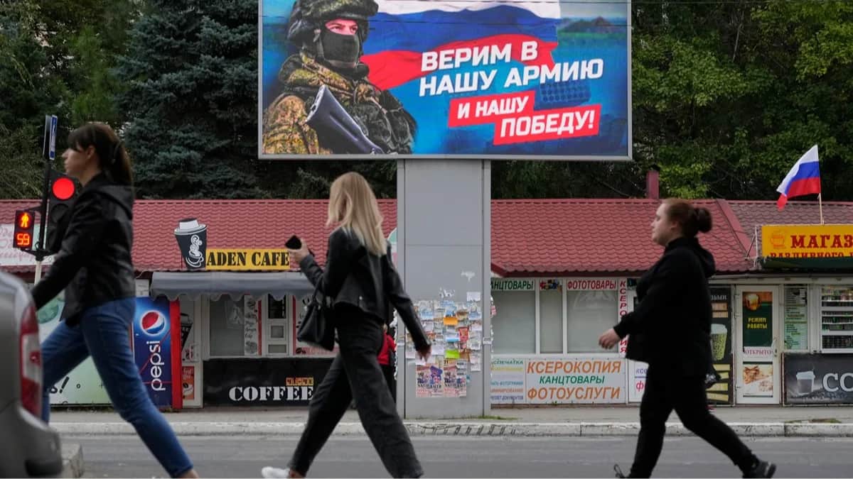Люди проходят мимо баннера с изображением военнослужащего и флага России в Луганске, Луганская область, Украина, 27 сентября 2022 года. Фото: AP Photo / Scanpix / LETA